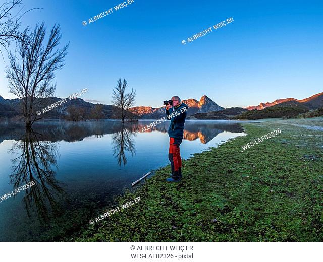 Spain, Asturias, Camposolillo, Cantabrian Mountains, senior man taking a photo at the seashore of Porma reservoir