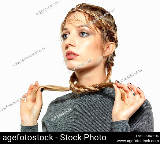 Portrait of beautiful young dark blonde woman. Female with creative braid hairdo on gray background. Girl holds braid ends in hands