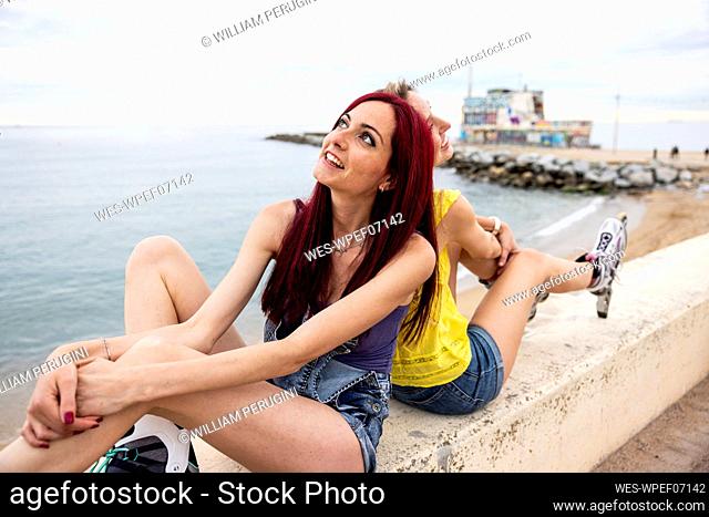 Thoughtful woman with friend sitting back to back by sea