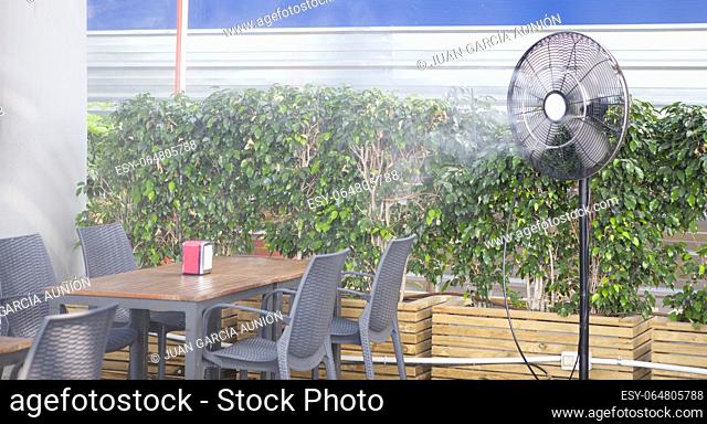 Water Vapour Mist Fan splashing vaporized water at terrace restaurant. Hospitality sector at summer