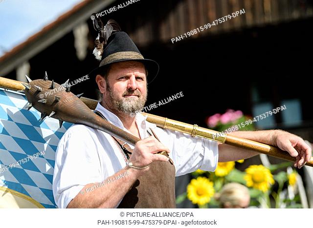 15 August 2019, Bavaria, Kochel Am See: As the historical ""blacksmith of Kochel"" a man with a Marien flag in the traditional costume procession goes to Maria...