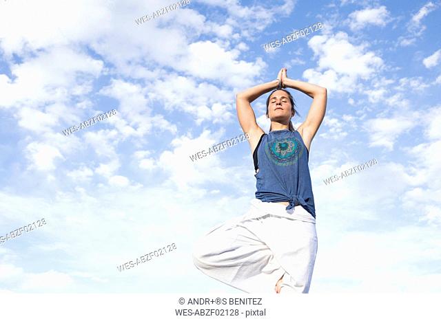Woman doing a yoga exercise under sky with clouds