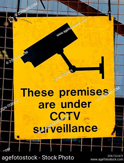 Yellow warning sign for CCTV surveillance using security cameras to secure a premises against crime on a wire mesh fence