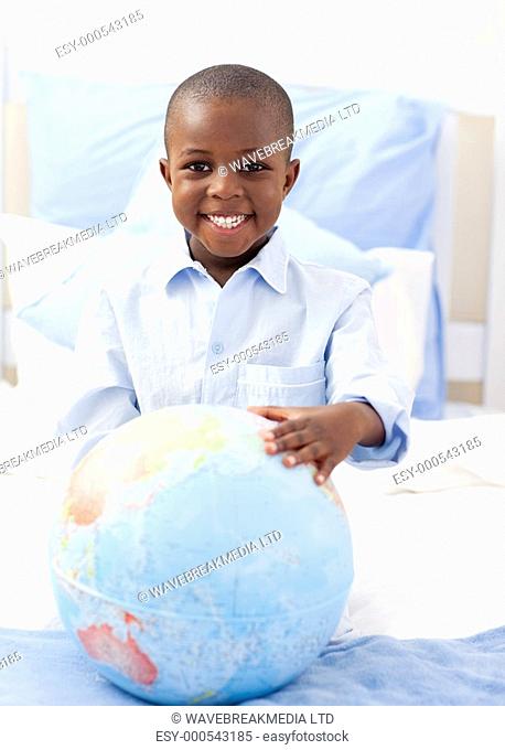 Cute little boy holding a terrestrial globe lying on his bed