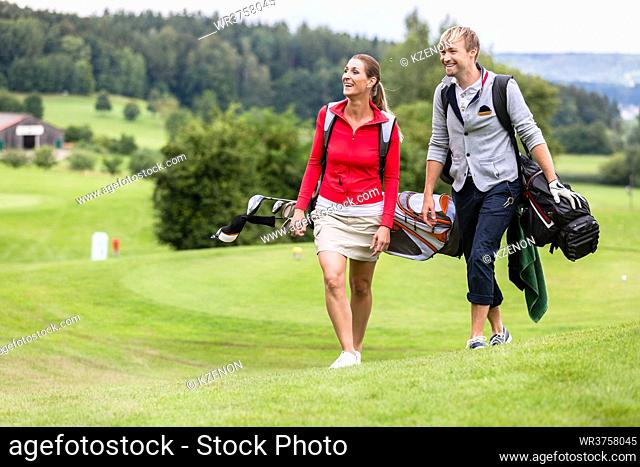 Happy sporty golfing couple walking together on golf course carrying their bags