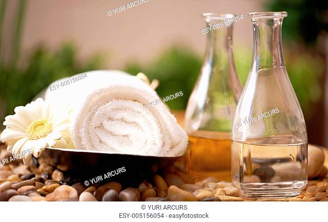 An spa arrangement consisting of a rolled hand towel and a daisy beside glass bottles