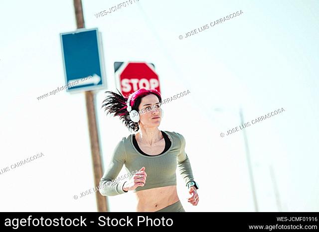 Woman with headphones looking away while running against sign board