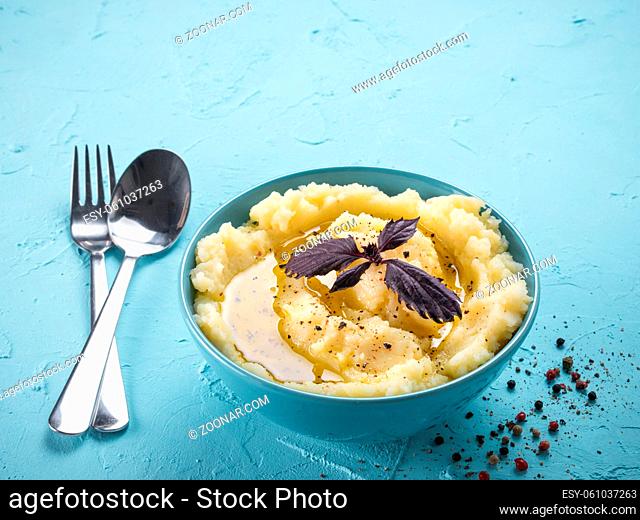 Mashed potatoes with fresh red basil, peppers and olive oil in blue bowl on blue concrete background. Copy space