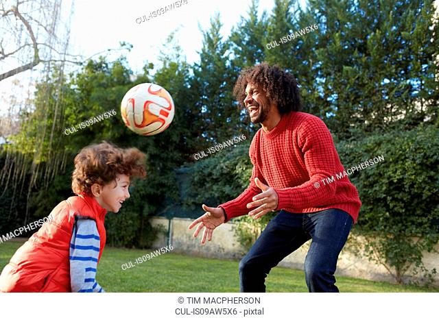 Father and son playing with football in garden smiling