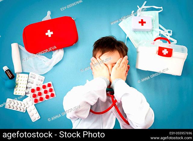 Child playing doctor in costume and mask. Boy holding pills with medical accessories around