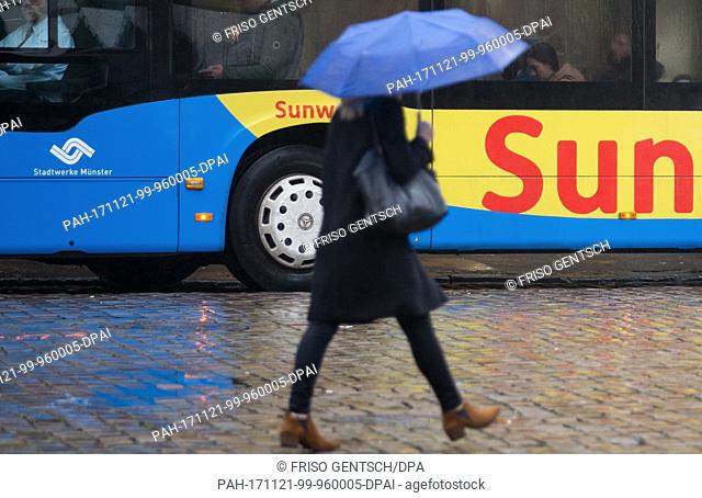 A pedestrian holding an umbrella crosses the street inÂ Muenster, Germany, 21 November 2017. A bus shows an advertisement for holiday in the sun in the...