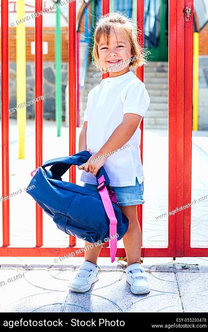 Blond-haired girl carrying a blue backpack at the entrance door of the school. School concept