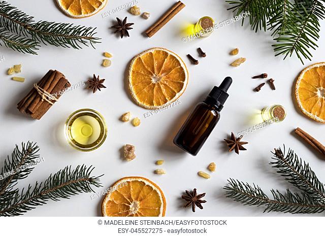 Selection of essential oils with Christmas spices and ingredients on white background: bottles of essential oil, spruce, fir, frankincense resin, star anise