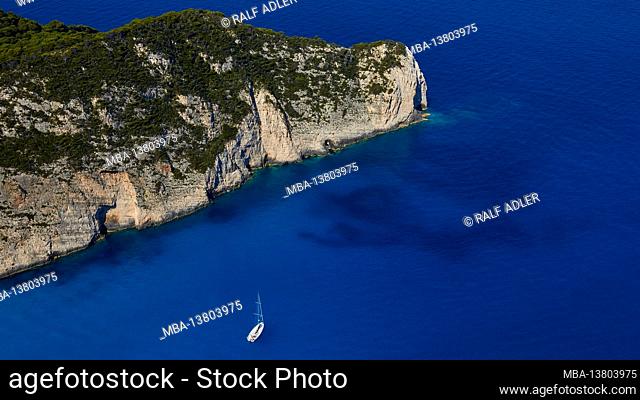 Zakynthos, Paralia Navagio, Shipwreck Beach, view of the north end of the bay, deep blue sea, crystal clear water, single white sailboat in the picture, no sky