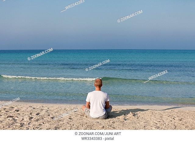 Junger sportlicher Mann macht sport yoga am Strand im Sand am meer in der Sonne
