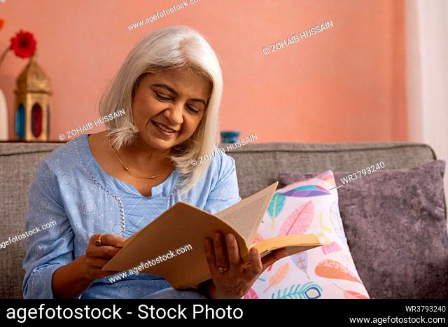 Portrait of old woman reading a book at home
