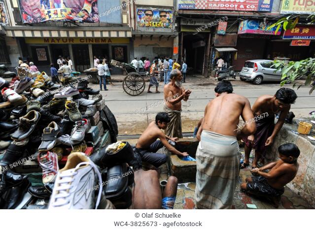 Kolkata (Calcutta), West Bengal, India, Asia - A group of men wearing a tradional longyi washes themselves at a public tap in the street next to a stall that...
