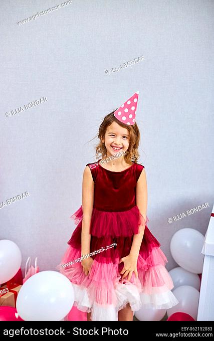 Cute, Joyful little girl in pink dress and hat play with balloons at home birthday party streamers, Happy birthday. Celebrating