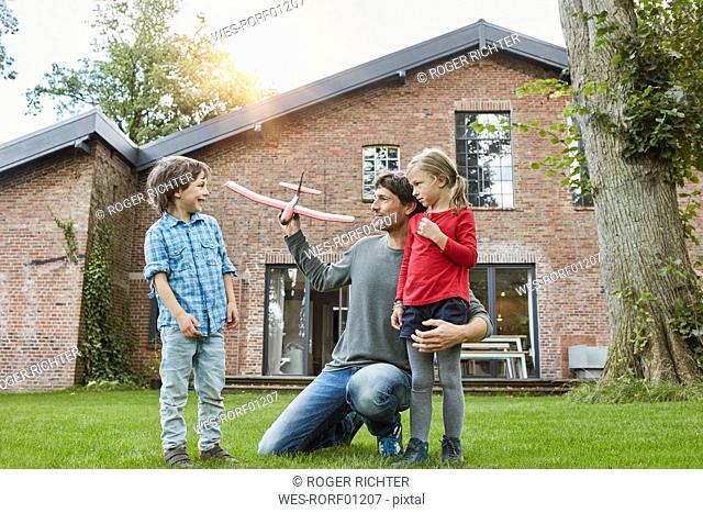 Father with two children playing with toy airplane in garden of their home