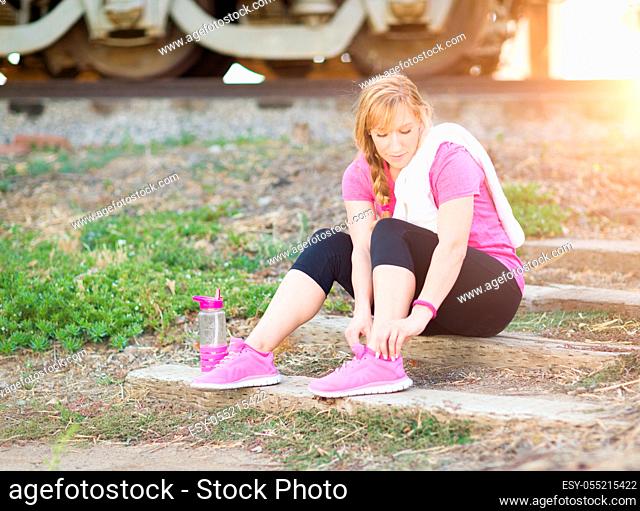 Young Adult Woman Outdoors With Towel and Water Bottle Tying Her Shoe Ready for Workout