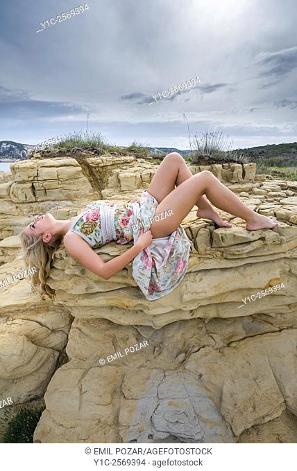 Younge woman lying on rock showing legs under long dress