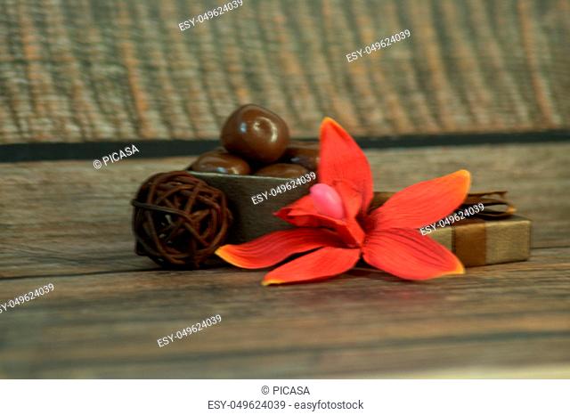 A box of chocolates, decorative balls, a bud of red orchid on a wooden table. Close-up
