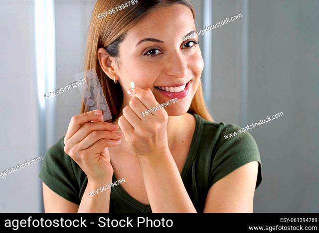 Close-up of smiling girl applying acne treatment anti-pickel patch on a pimple in bathroom at home