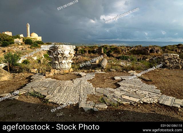 Pillar and ancient street in sunlight during storm in ruins with dramatic cloudscape with mosque in Tyre, Sour, Lebanon