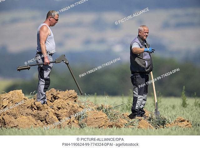 24 June 2019, Hessen, Ahlbach: Using metal probes and spades, experts from the explosive ordnance clearance service examine a huge crater on a field