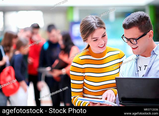 Two students using modern technology stand in the hallway while waiting for classes to begin