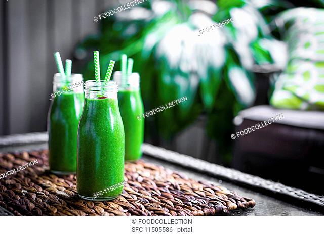 Fresh green smoothie in glass bottles with straws