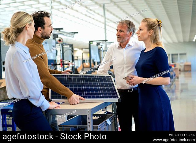 Businessman holding solar panel discussing with colleagues at industry