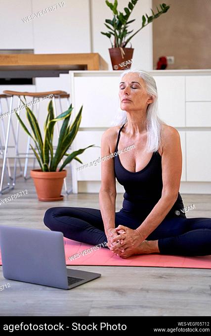 Fit mature woman doing stretching exercise with laptop at home