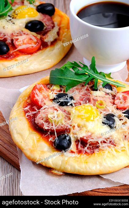 Mini pizza with sausage and egg and arugula, a cup of coffee