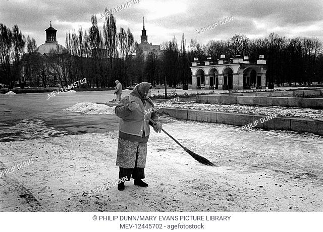 A woman street sweeper brushes snow in a Warsaw park, Poland