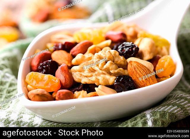 Healthy trail mix snack made of nuts (walnut, almond, peanut) and dried fruits (raisin, sultana) on spoon (Selective Focus, Focus one third into the spoon)