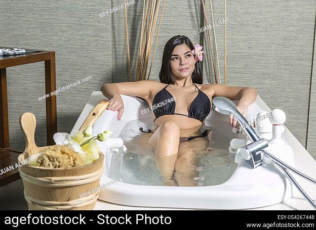 Sensual young brunette in bikini lying in recreation bath enjoying massage center