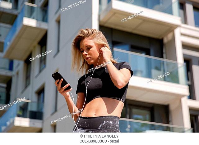 Young woman listening to music on mobile phone, building in background