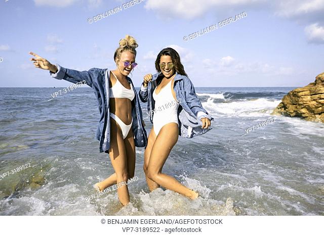 Two women jumping in sea water at beach, Chersonissos, Crete, Greece