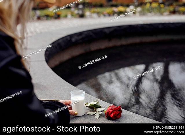 Woman placing rose and candle on fountain edge