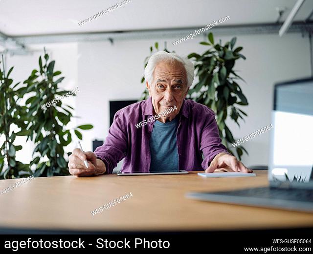 Senior businessman using digital tablet while sitting by table at office