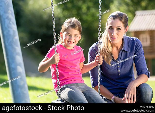Woman with laughing girl on playground swing having fun together