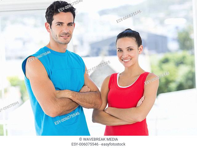 Fit couple with arms crossed in bright exercise room