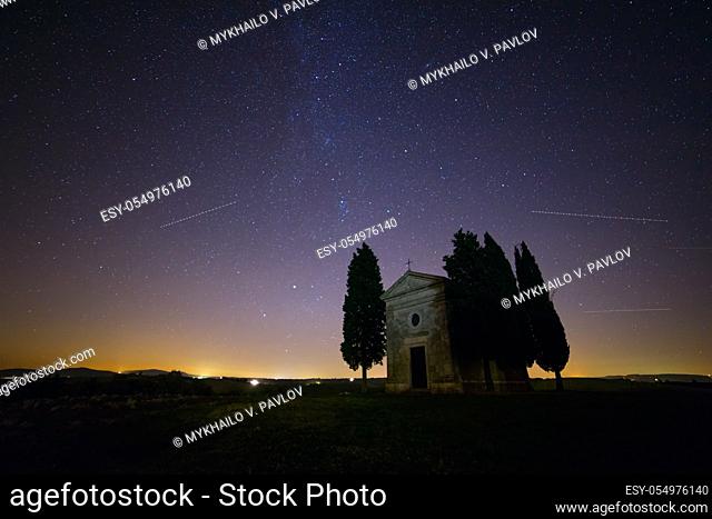 Italy. Tuscany. Lonely chapel and cypress trees in a field. Night sky with myriads of stars