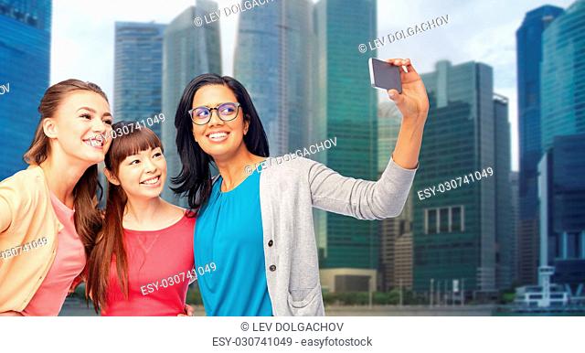 travel, tourism and people concept - international group of happy smiling different women taking selfie with smartphone over singapore city skyscrapers...
