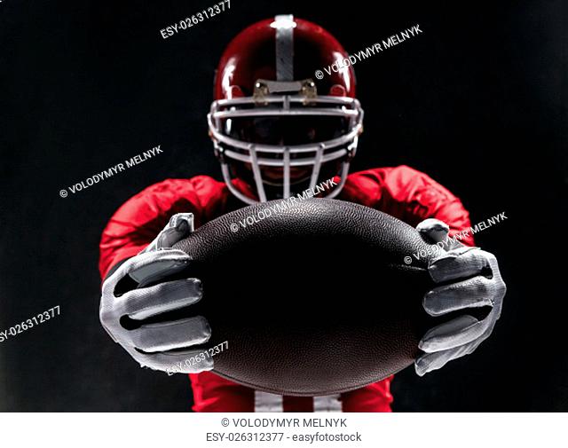 Caucasian fitness man as american football player holding a ball on black background