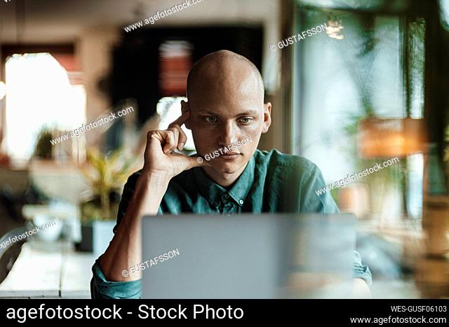 Thoughtful bald male cafe owner using laptop