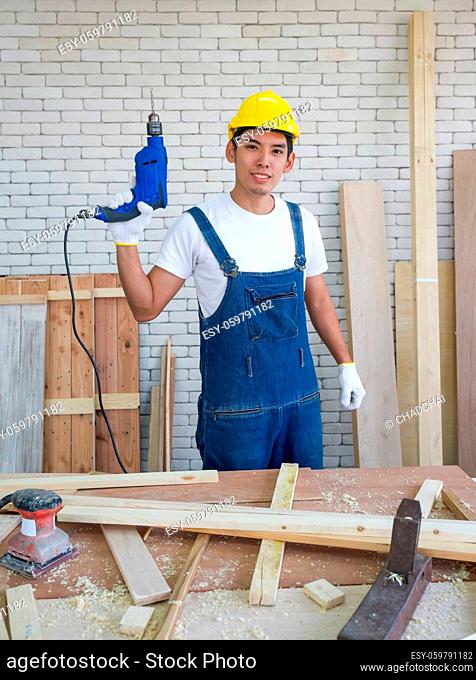 Asian carpenter wearing a yellow hardhat, poses confidently before beginning the job of receiving orders at the wood working place