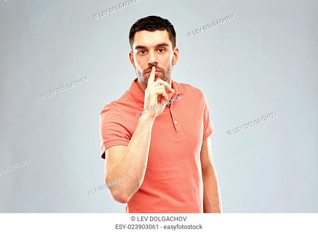 silence, gesture and people concept - serious young man making hush sign over gray background