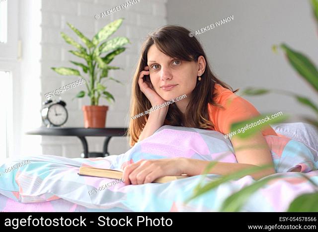 The girl at home in bed reads a book and looked distracted